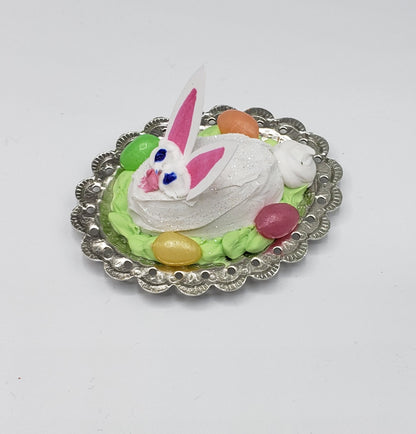 Fashion Doll size Easter bunny cake with white frosting and colorful candy eggs on a silver decorative plate