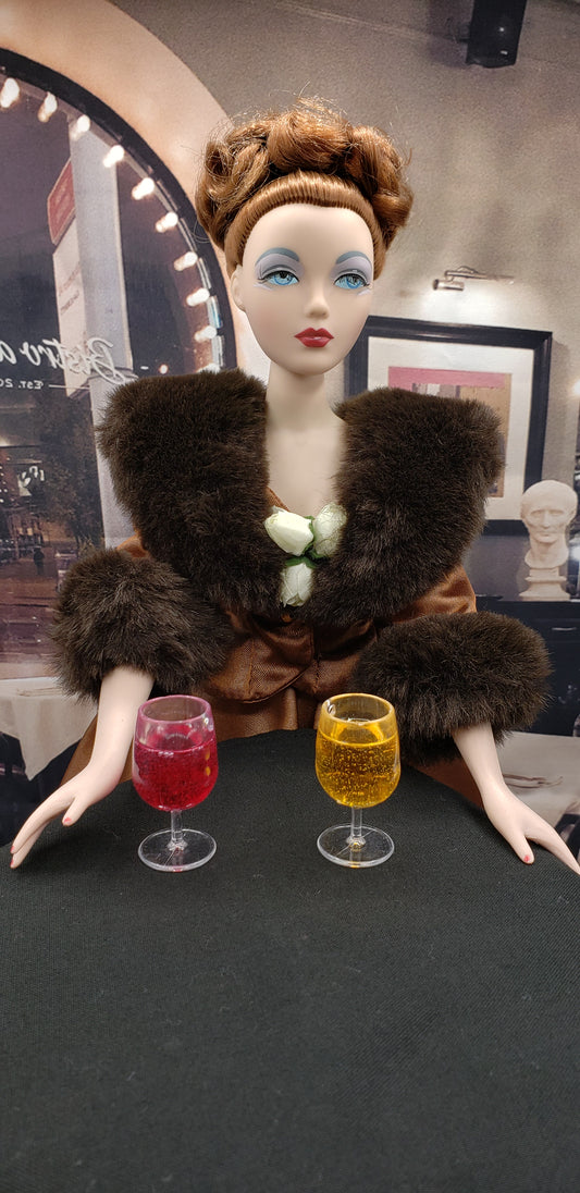 Gene doll with styled brown hair and fur outfit holding two miniature wine glasses as dollhouse accessories