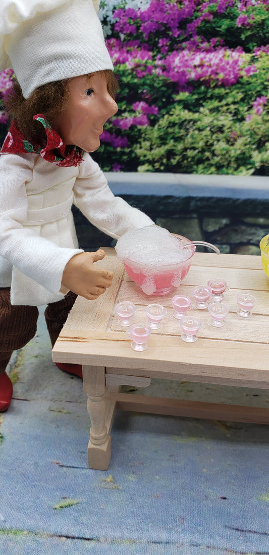 Chef doll serving miniature dollhouse party punch in a clear pink bowl with matching tiny glasses on a wooden table