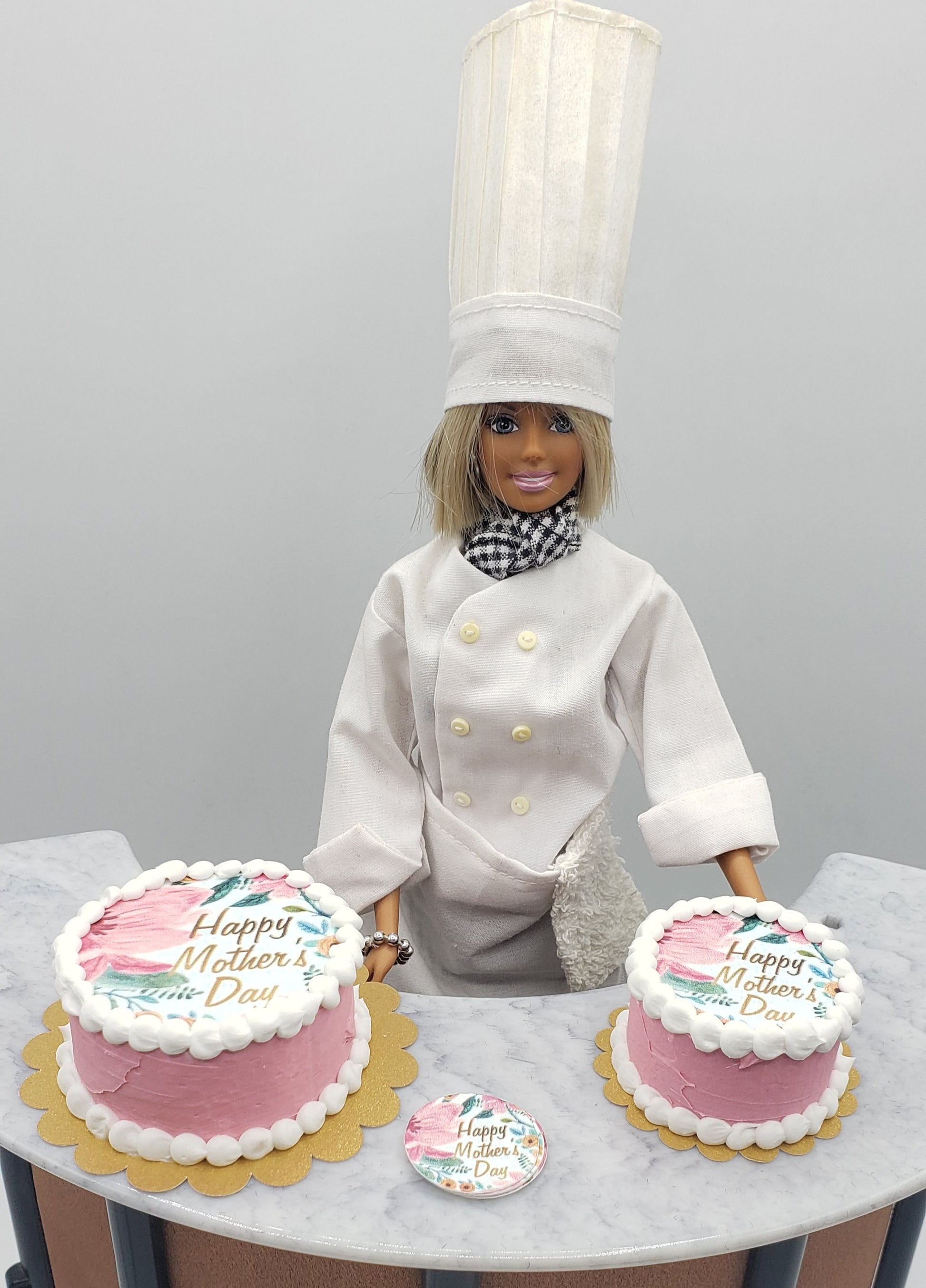 Chef doll presenting two miniature Mother's Day cakes decorated with pink frosting and celebration messages